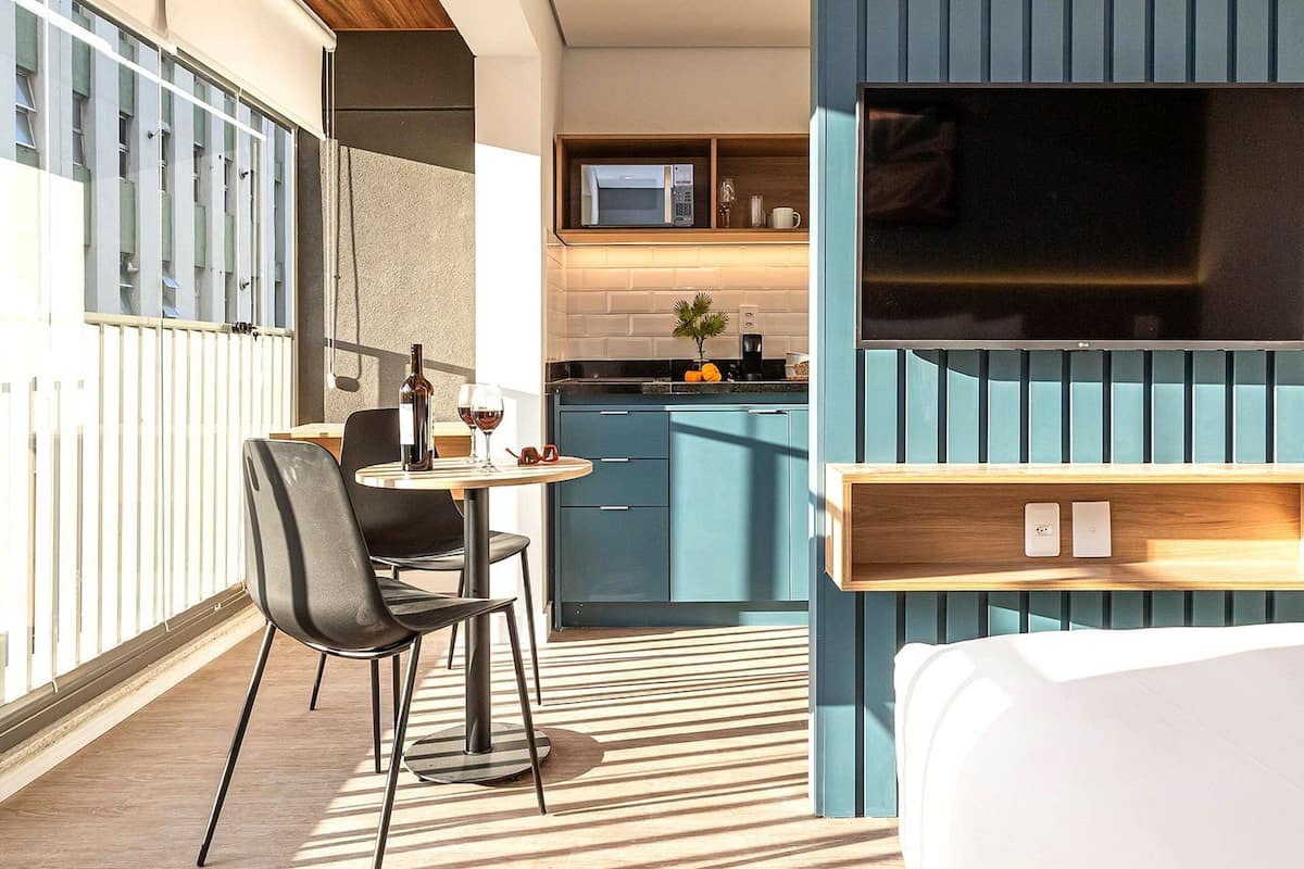 Une chambre d’hôtel moderne équipée d’un lit, d’un coin repas avec une table et des chaises, d’un coin cuisine et d’un grand téléviseur fixé au mur.