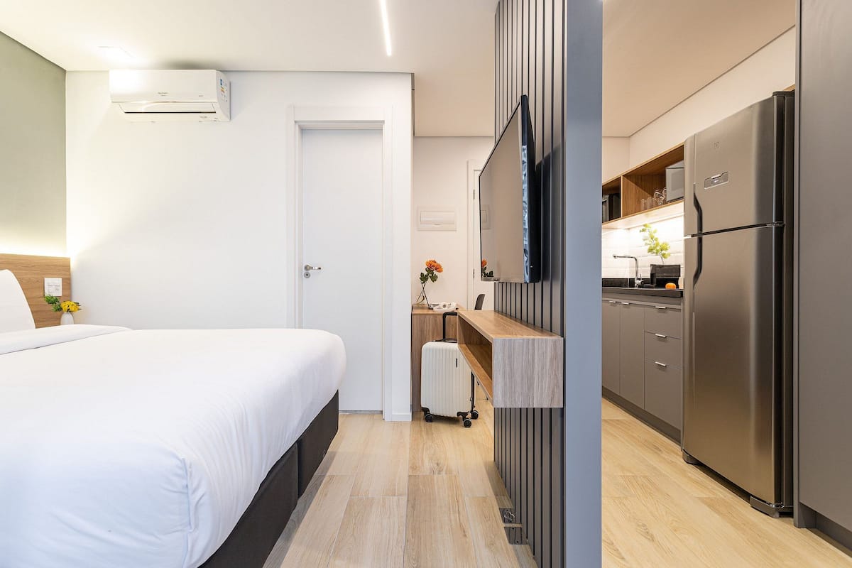Une chambre d’hôtel équipée d’un lit, d’un bureau, d’une kitchenette avec réfrigérateur et d’un appareil de climatisation.