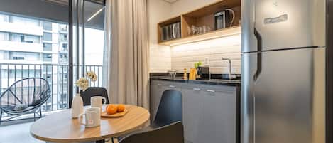 A modern kitchen with a large refrigerator, a dining table with chairs, and a view of the city through large windows.