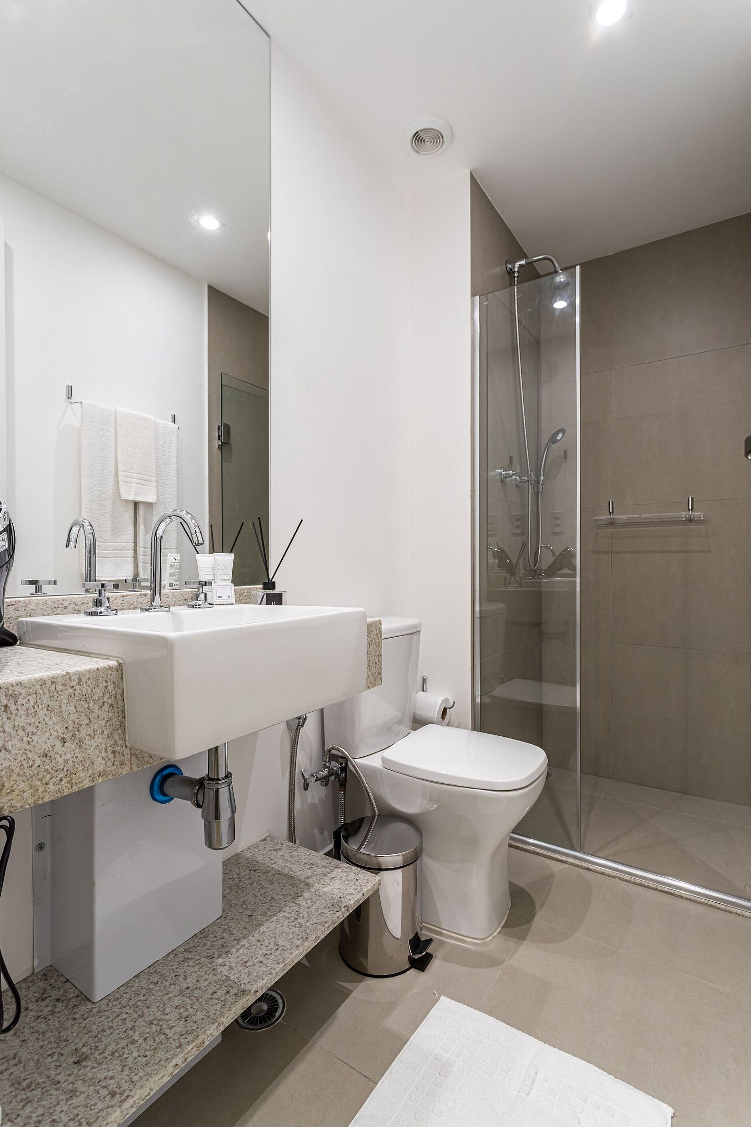 A modern bathroom with a glass-enclosed shower, a white sink, and a toilet.