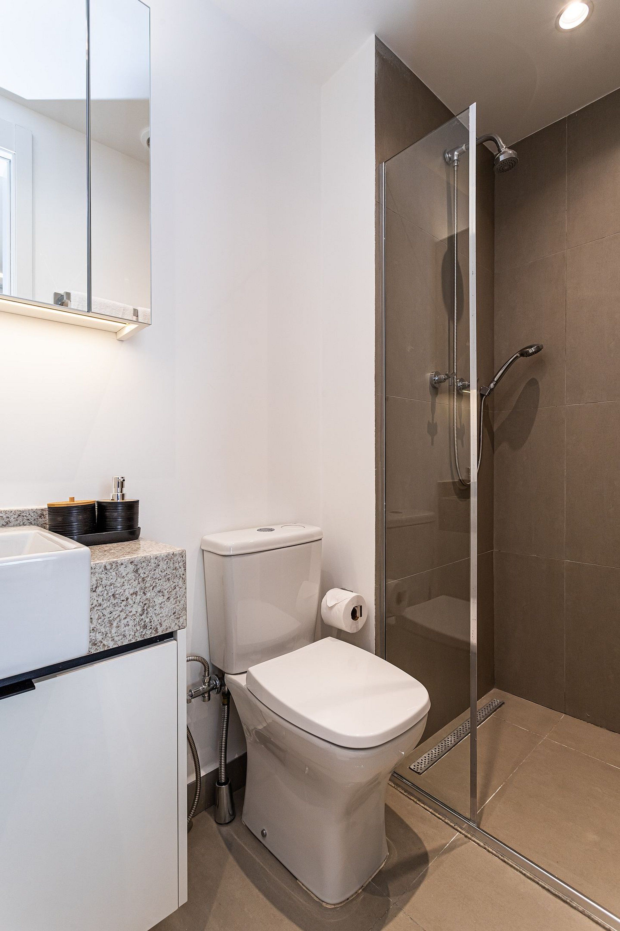 Ein modernes Badezimmer mit einer gläsernen Duschkabine, Toilette und Waschbecken mit Marmorplatte.