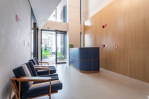 A reception area with a counter, seating, and a view of the outside. - Pivô Pamplona by Viva - Apartamentos novos e espaçosos ao lado da Av Paulista (São Paulo)