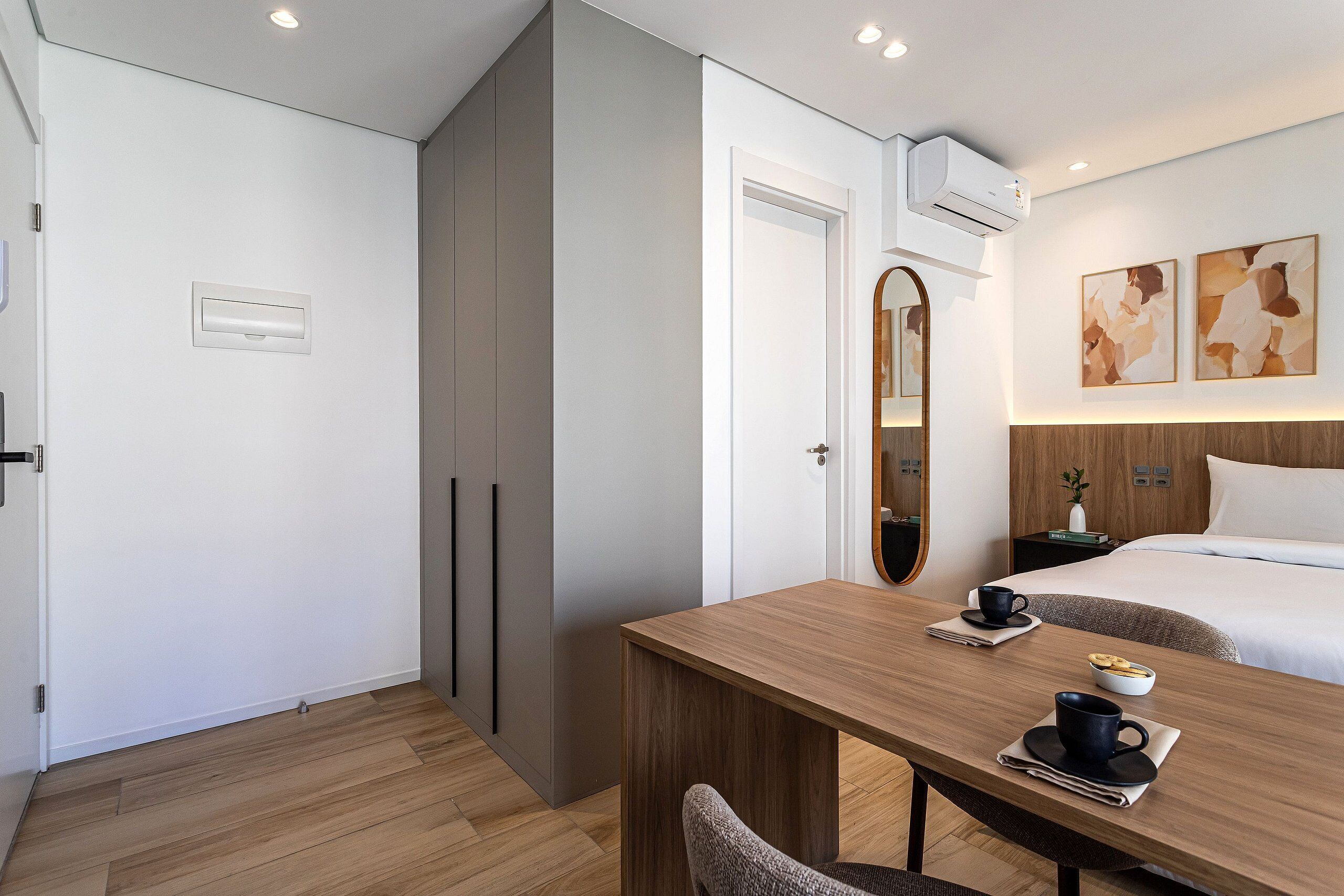 Habitación de hotel con una mesa de madera, cama, espejo y obras de arte en la pared.