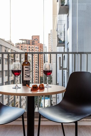A round table with two wine glasses and a bottle of wine, two black chairs, and a pair of sunglasses on the table. - Pivô Pamplona by Viva - Apartamentos novos e espaçosos ao lado da Av Paulista (São Paulo)