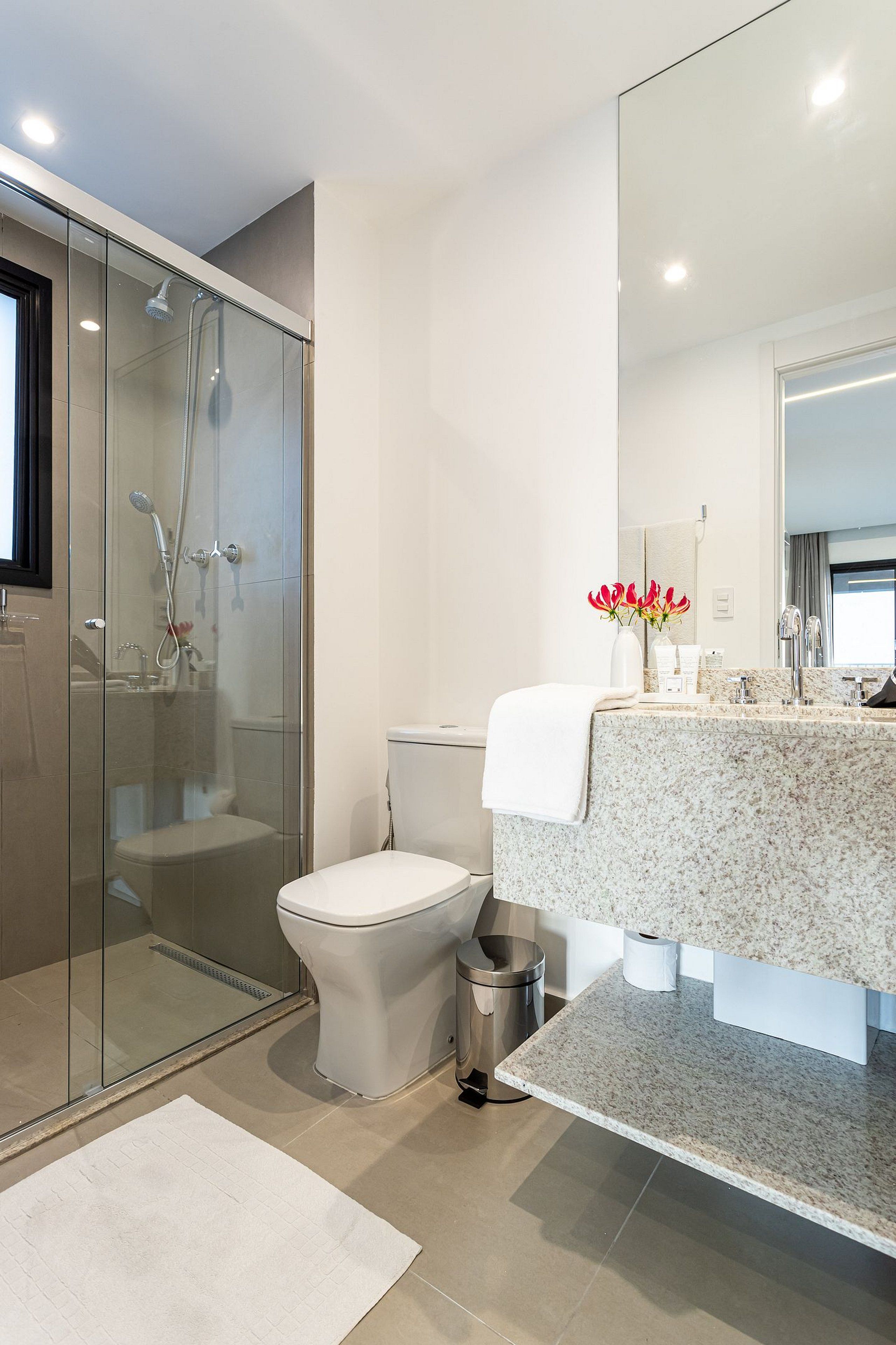 Une salle de bain moderne avec une douche à parois de verre, des toilettes, un lavabo en marbre et un miroir.