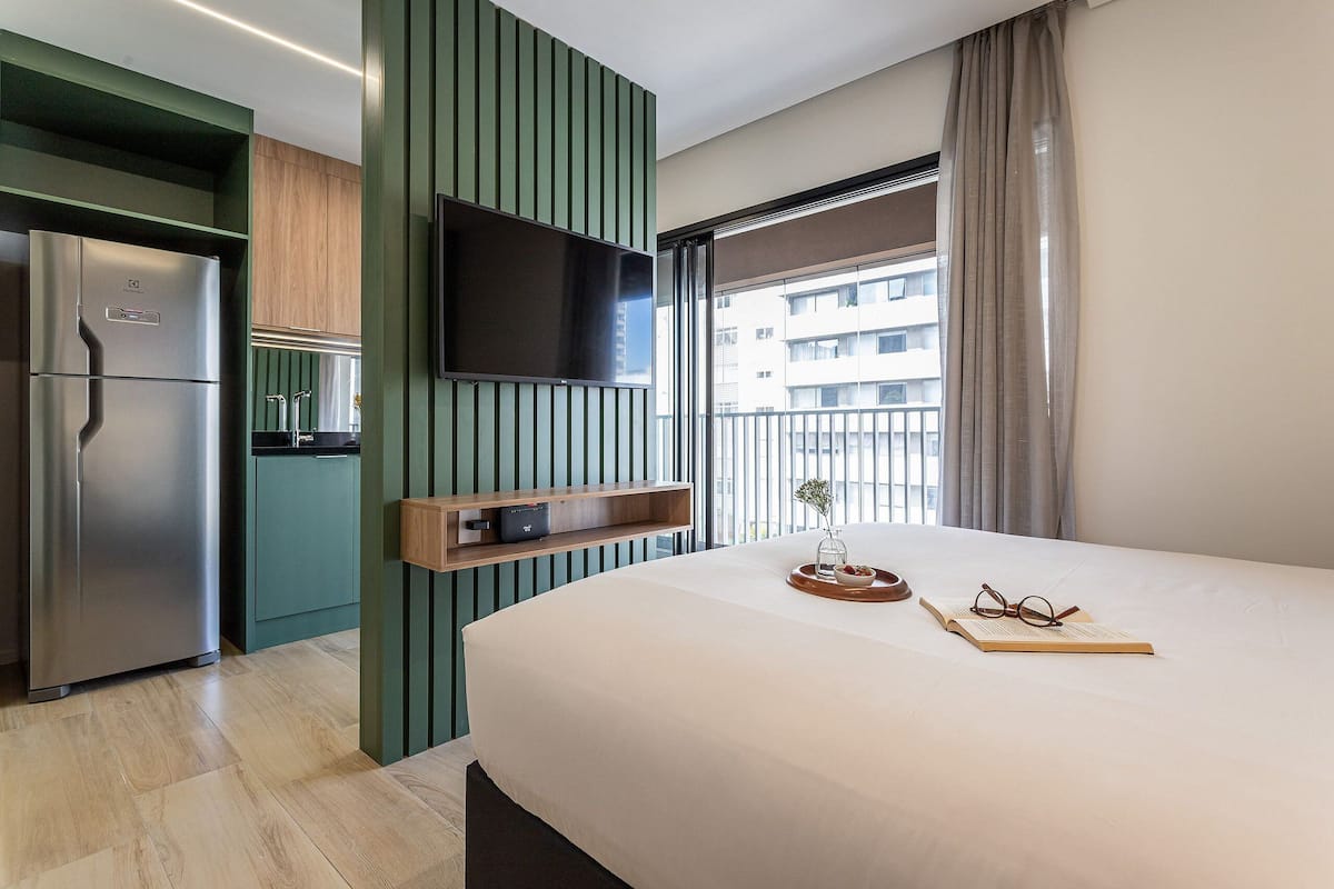 Une chambre d’hôtel moderne équipée d’un lit, d’une télévision, d’un coin cuisine et d’un balcon avec vue.