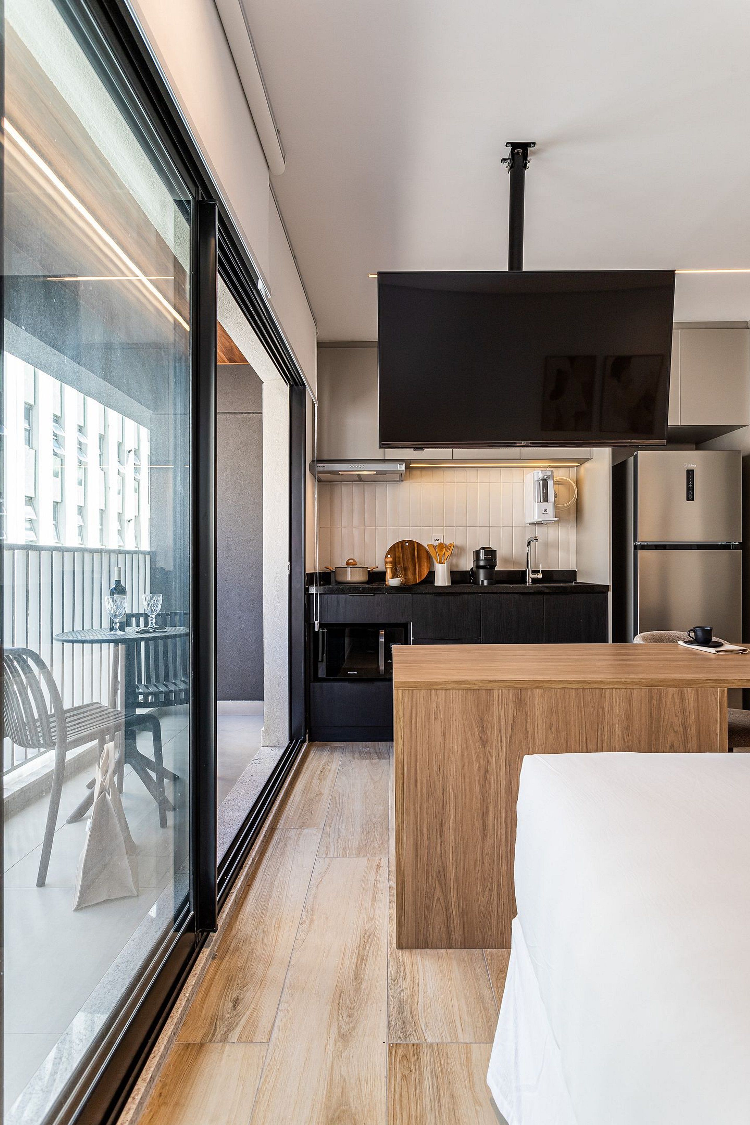 A modern kitchen with a large window, a flat-screen TV, and a wooden dining table.