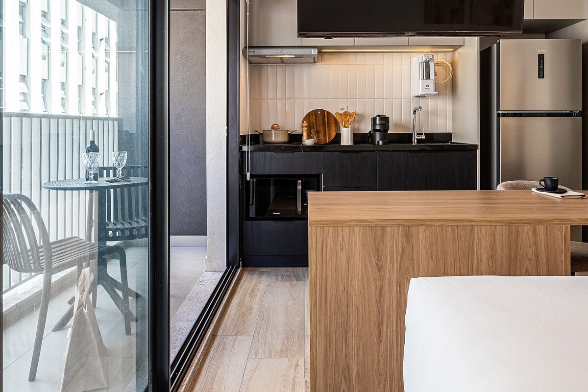 A modern kitchen with a large window, a flat-screen TV, and a wooden dining table.