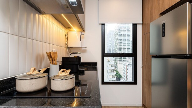 A modern kitchen with a stainless steel refrigerator, a window with a city view, and a countertop with pots and utensils.