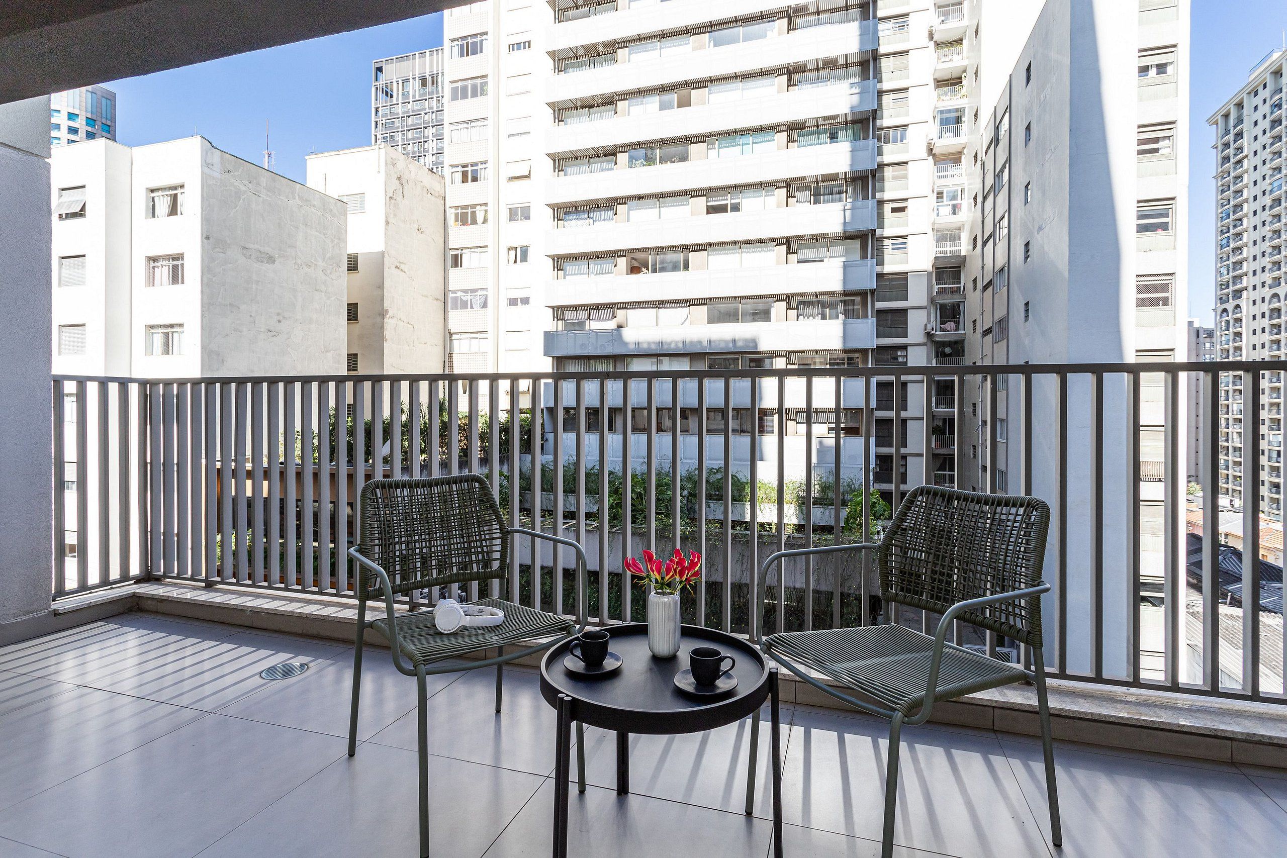 A balcony with two chairs, a small table, and a vase with flowers.