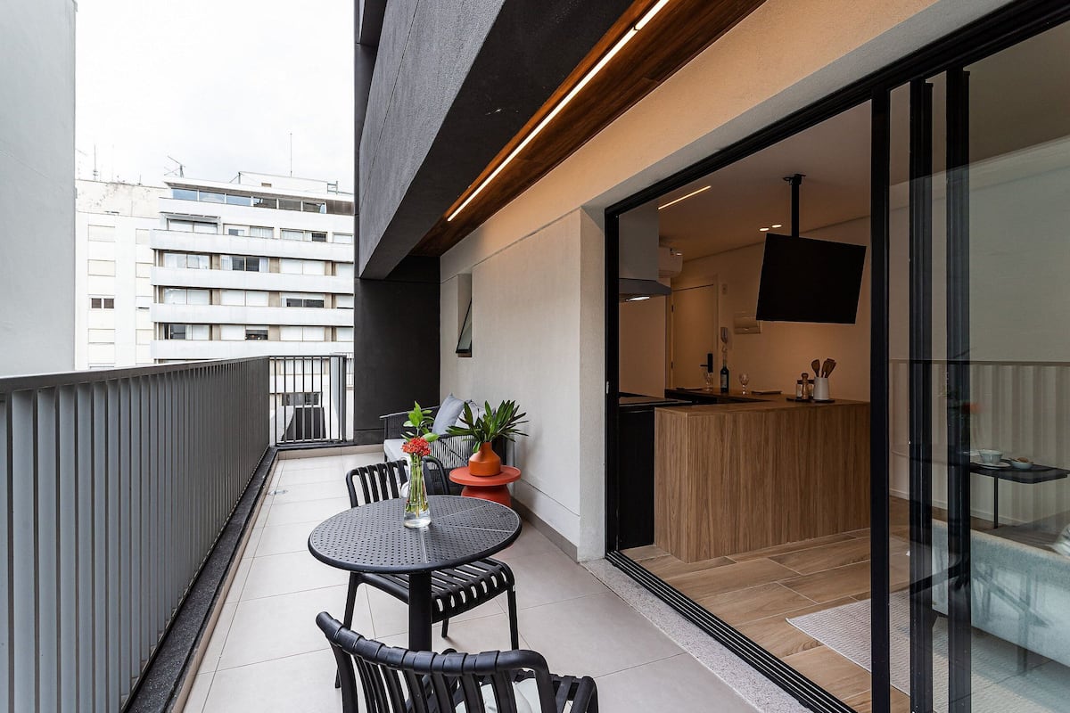 Un balcon avec une table ronde et des chaises, une plante en pot, et une vue sur un bâtiment en arrière-plan.