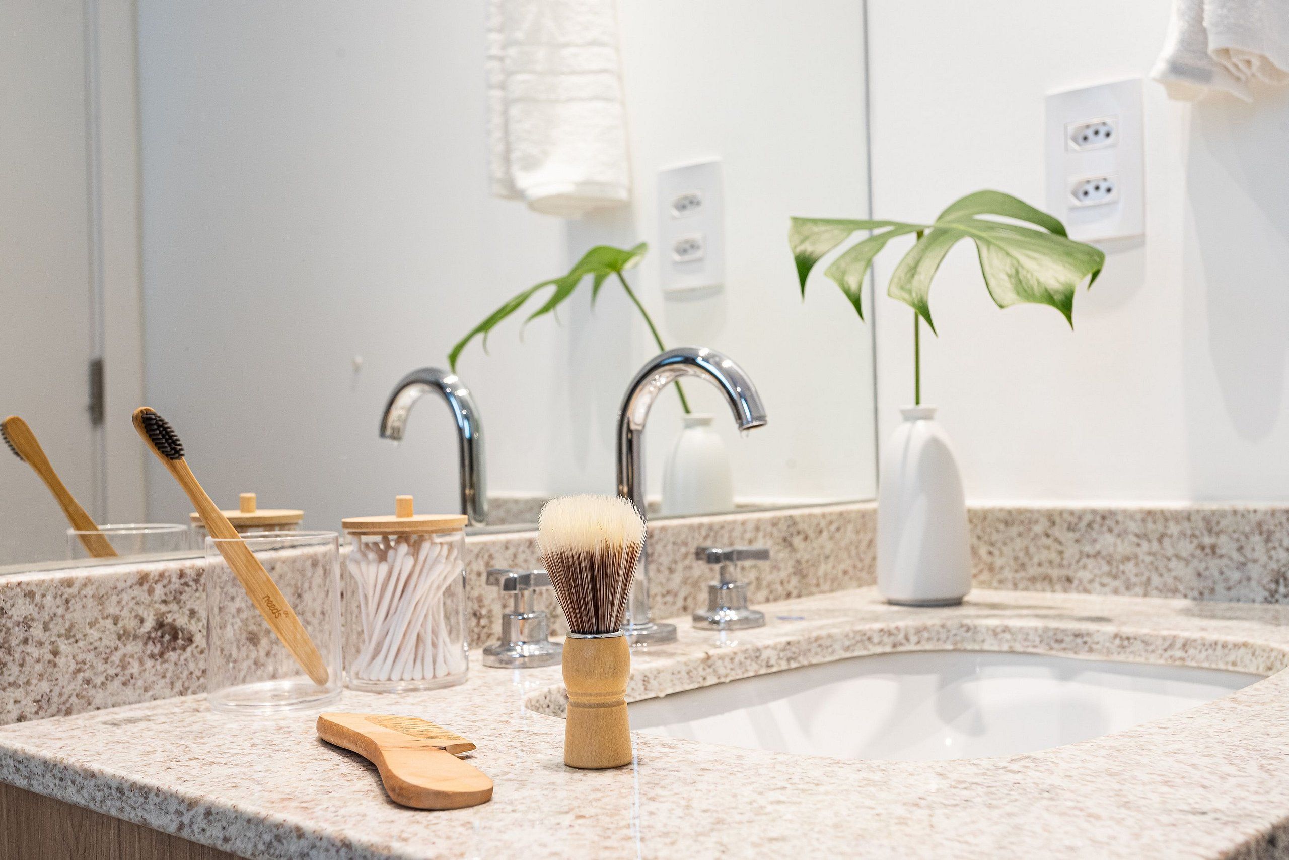 A bathroom with a granite countertop, a sink, a mirror, a plant, and grooming tools.