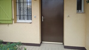 A beige building with a brown door, a green shutter, and a window with a metal grill. - 1-bedroom studio with sea view. Ideal for 2 adults and 1 child. (Saint Pierre la mer)