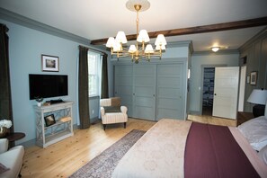 A bedroom with a large bed, a television on a side table, a chair, and a wardrobe.