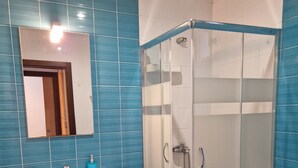 Une salle de bain avec des carreaux bleus, un lavabo blanc, un miroir, une douche en verre et des toilettes.