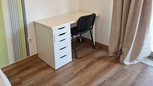Une petite pièce, bien rangée, avec un bureau, une chaise et une fenêtre agrémentée de rideaux.