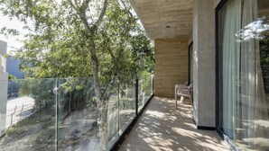 Un balcon moderne avec une balustrade en verre, un banc et une vue sur des arbres et une rue.