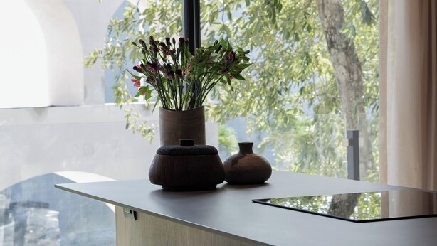 Une cuisine moderne avec une grande fenêtre, des tabourets en bois et une plante en pot.