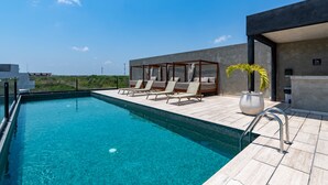Un espace piscine extérieur moderne, doté de chaises longues et d’une pergola, le tout entouré d’un immeuble de grande hauteur.