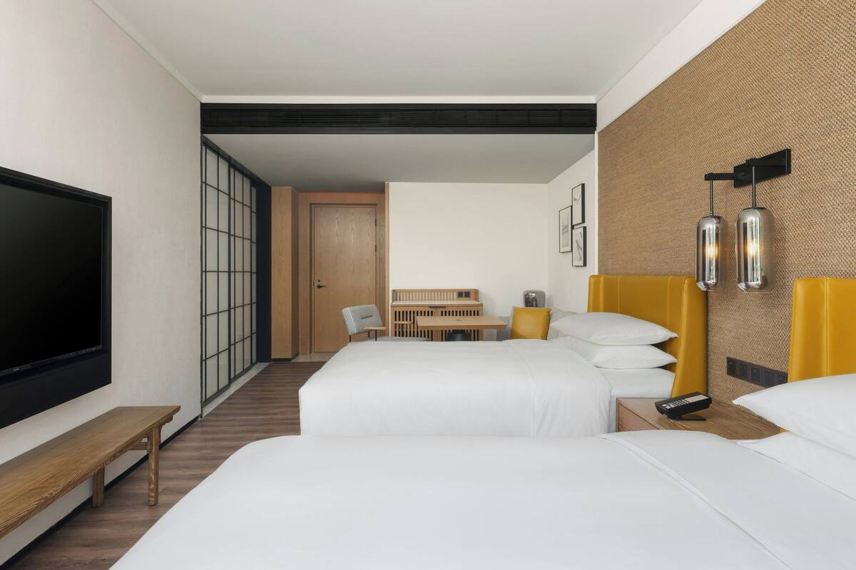 A hotel room with two beds, a TV, a desk, and a seating area.