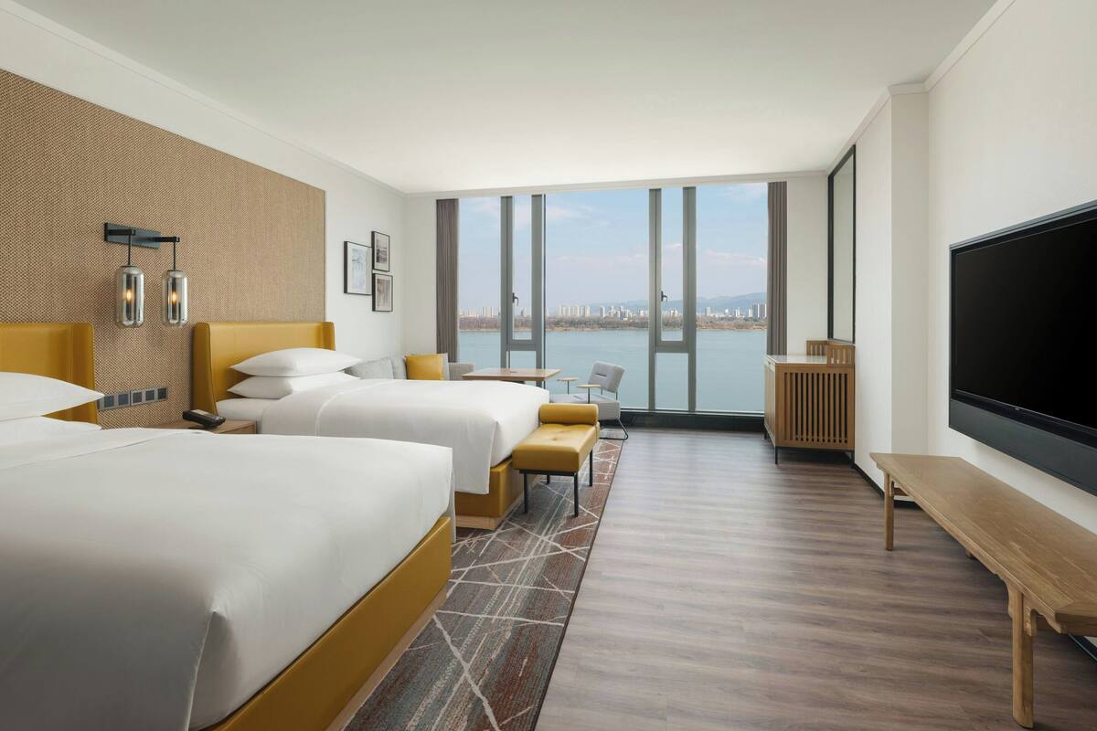 A hotel room with two beds, a large TV, and a view of a body of water.