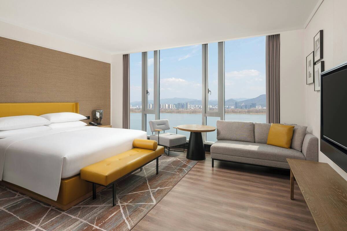A hotel room with a large bed, a sofa, a small table, and a TV.