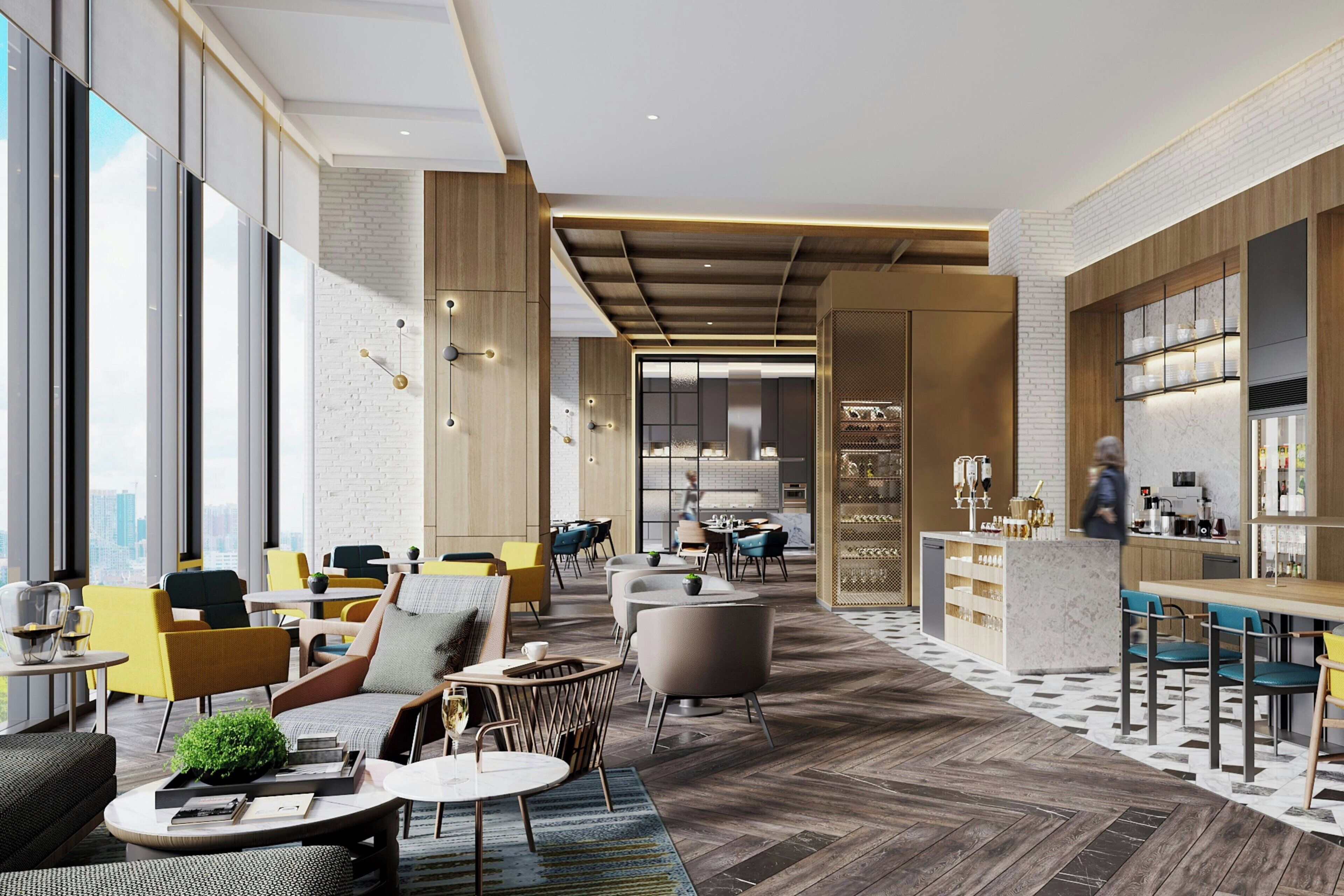A modern hotel lobby with a mix of seating areas, a bar, and a kitchen visible in the background.