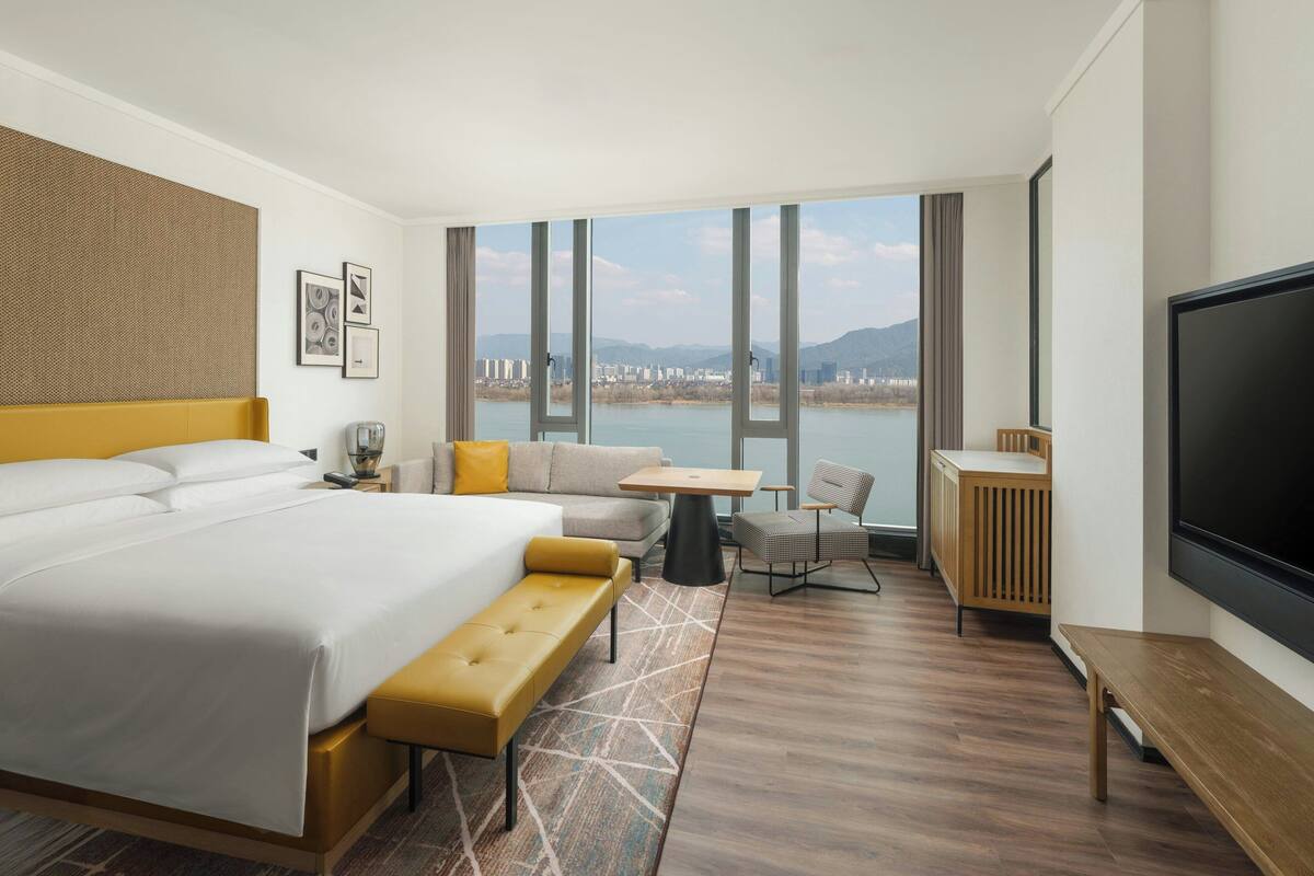 A modern hotel room with a large bed, a sofa, a small table, and a TV.