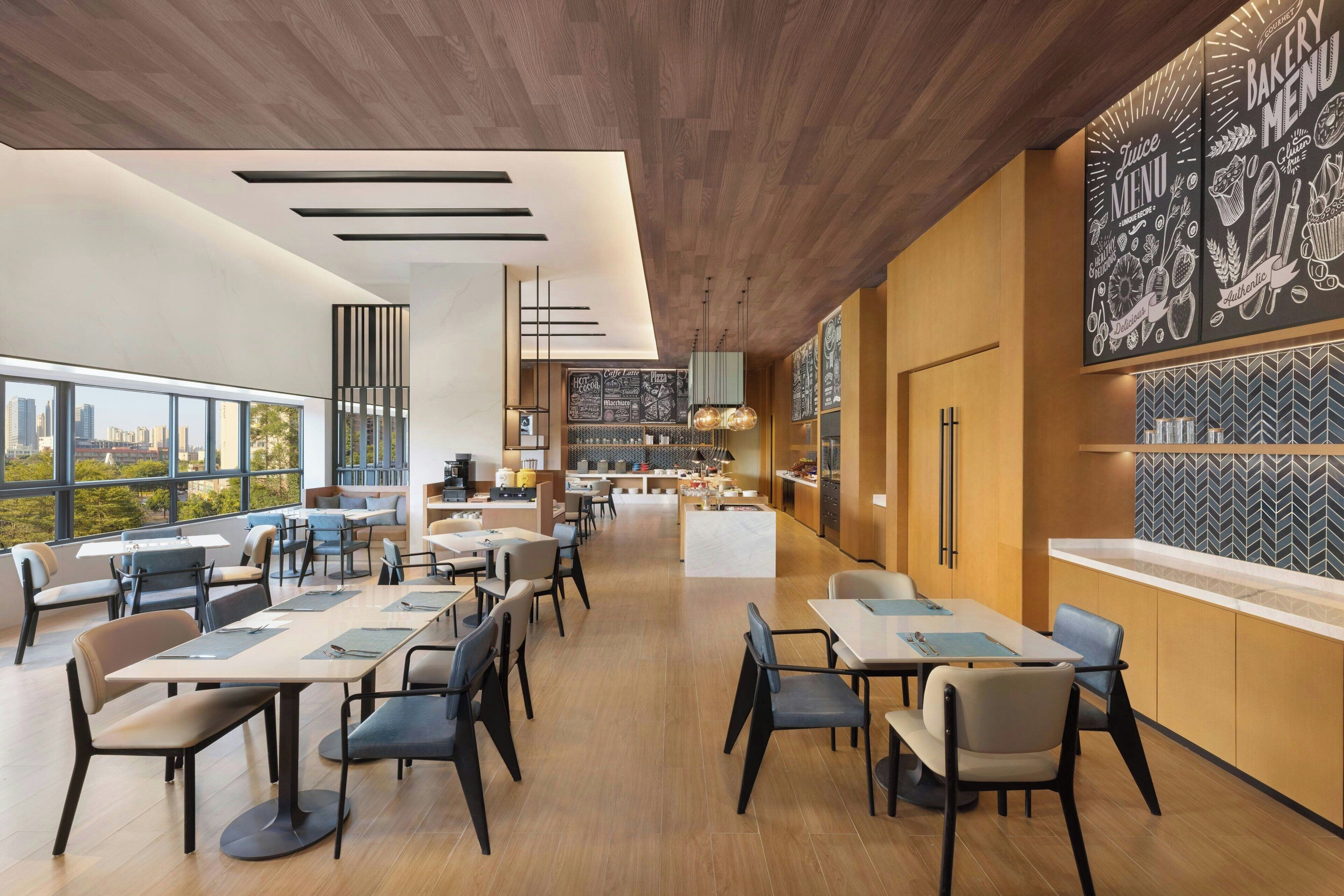 A modern restaurant with high ceilings, large windows, and a central kitchen area.