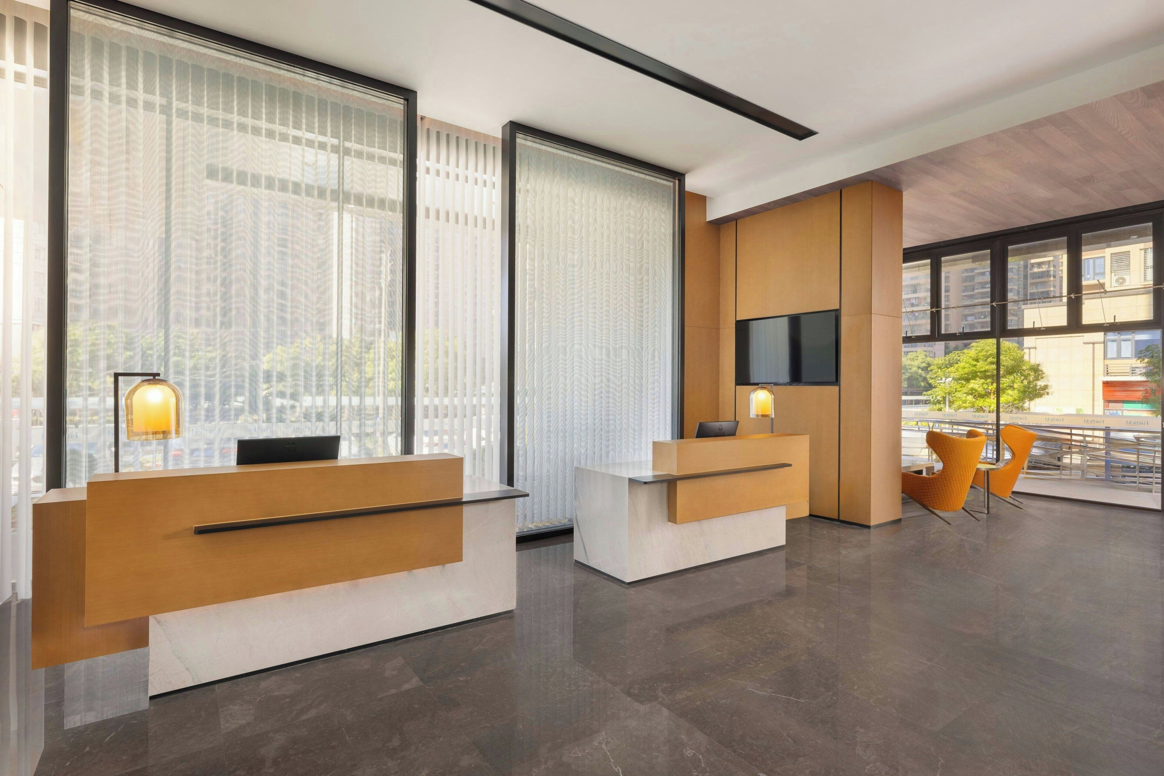 A modern reception area with two reception desks, a flat-screen TV, and a seating area with yellow chairs.