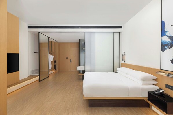 Una habitación de hotel moderna con una cama grande, una mesita de noche con teléfono, televisor y espejo.