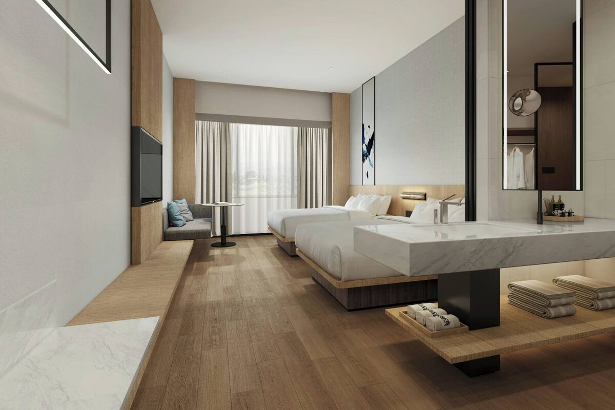 A modern hotel room with a large bed, a sitting area, a TV, a bathroom with a mirror, and a large window.