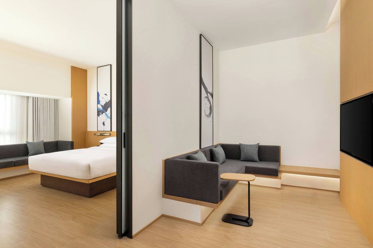A modern hotel room with a bed, a sofa, a small table, and a TV.