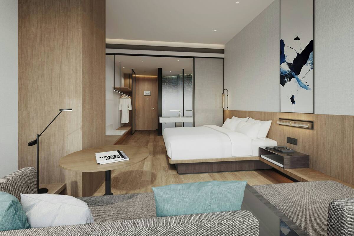 A modern hotel room with a bed, a small table, a sofa, and a painting on the wall.