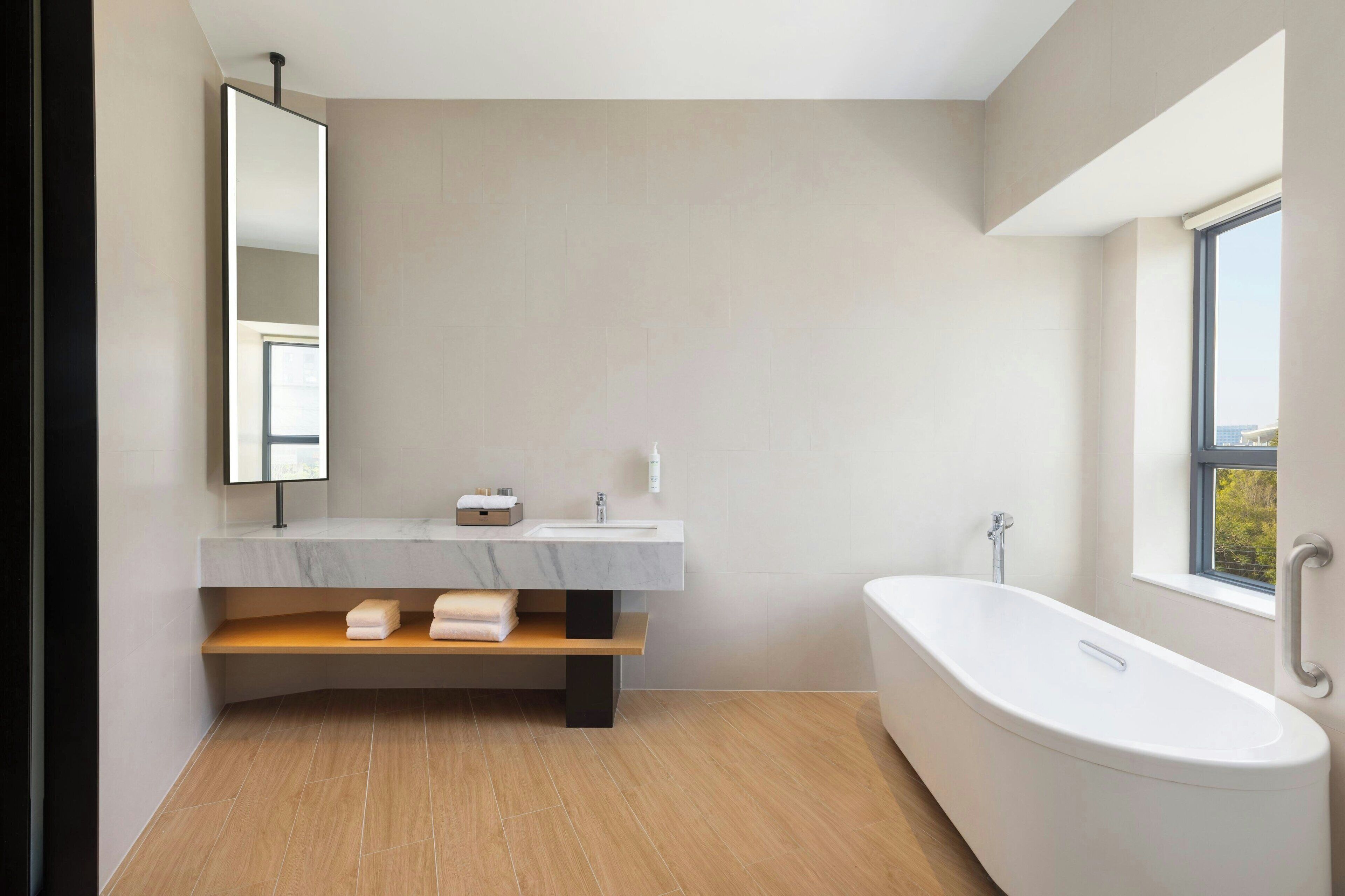 Een moderne badkamer met een marmeren wastafel, een vrijstaand bad en een grote spiegel.