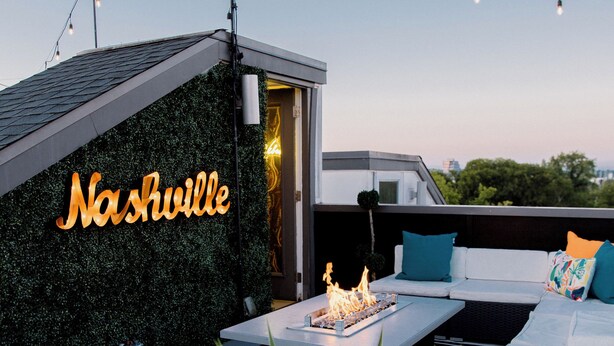 Une terrasse sur le toit, agrémentée d’un panneau lumineux au néon indiquant « Nashville », d’un foyer et d’un espace salon avec des coussins.