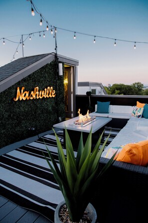 A rooftop terrace with a neon sign reading "Nashville," a fire feature, and a seating area with cushions. - Rooftop Home with Skyline Downtown Views (Nashville)