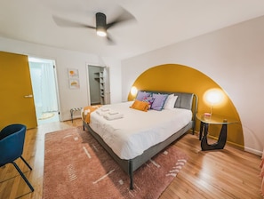 Un dormitorio moderno con cama, una silla azul, una mesa de vidrio y un diseño de pared curvo único.