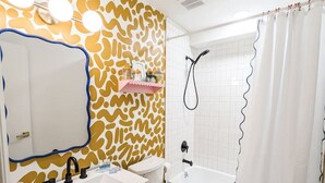 A modern bathroom with a patterned wall, a double sink vanity, a toilet, a bathtub, and a shower curtain.