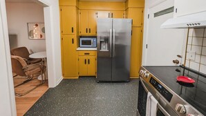 A compact kitchen with yellow cabinets, a stainless steel refrigerator, a microwave, and a stove.