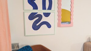 A room with a brown chair, a framed abstract artwork, and a mirror with a wavy frame.