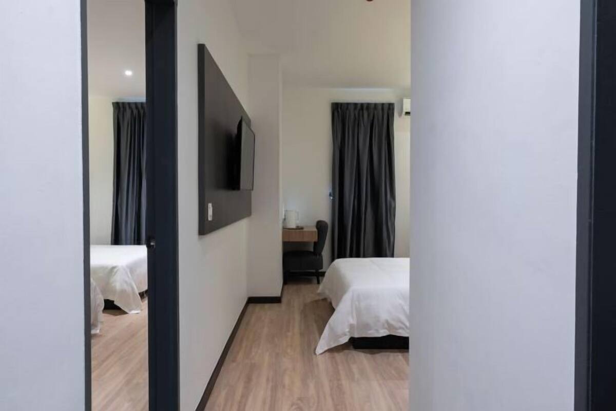 A hotel room with two beds, a flat-screen TV mounted on the wall, a desk with a chair, and a window with curtains.