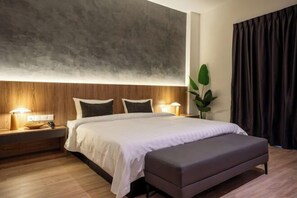 A modern bedroom with a wooden headboard, a large bed with white bedding, a bedside table with a lamp, and a dark curtain. - Blu Sentral Hotel (Tawau)