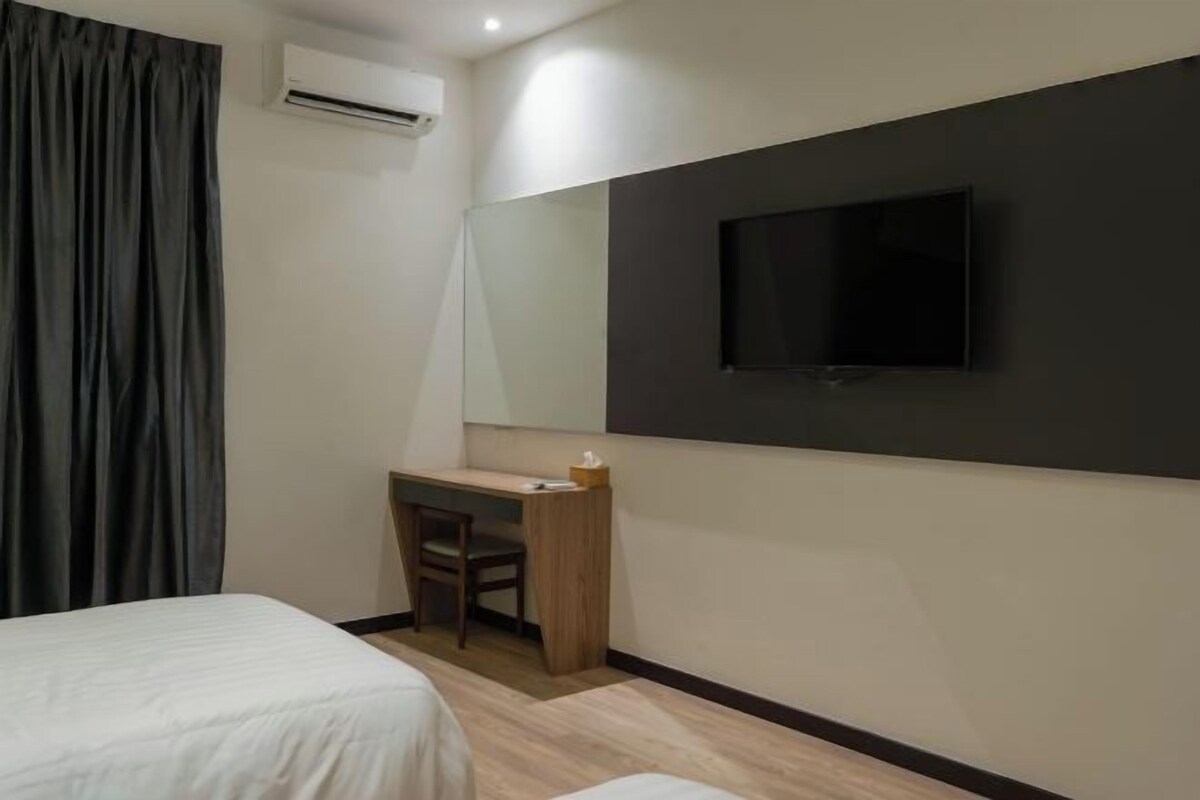 A hotel room with a bed, a desk with a chair, a television mounted on the wall, and an air conditioning unit.