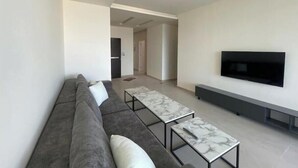 Ein modernes Wohnzimmer mit einem grauen Sofa, zwei Couchtischen mit Marmorplatten, einem an der Wand montierten Flachbildfernseher und einem minimalistischen Design.