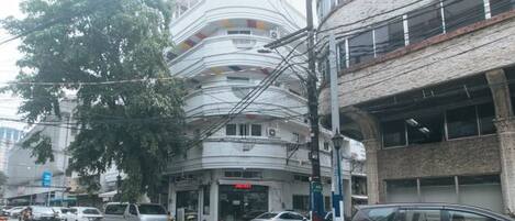 Un edificio de varios pisos con fachada curva, coches aparcados y señalización visible.