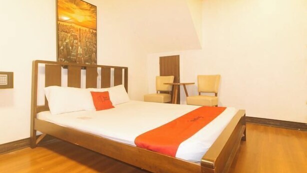 A neatly made bed with a wooden frame, a white mattress, and a red blanket. There is a small round table with a chair beside the bed. - RedDoorz at Emperor Manila Boutique Hotel (City of Manila)