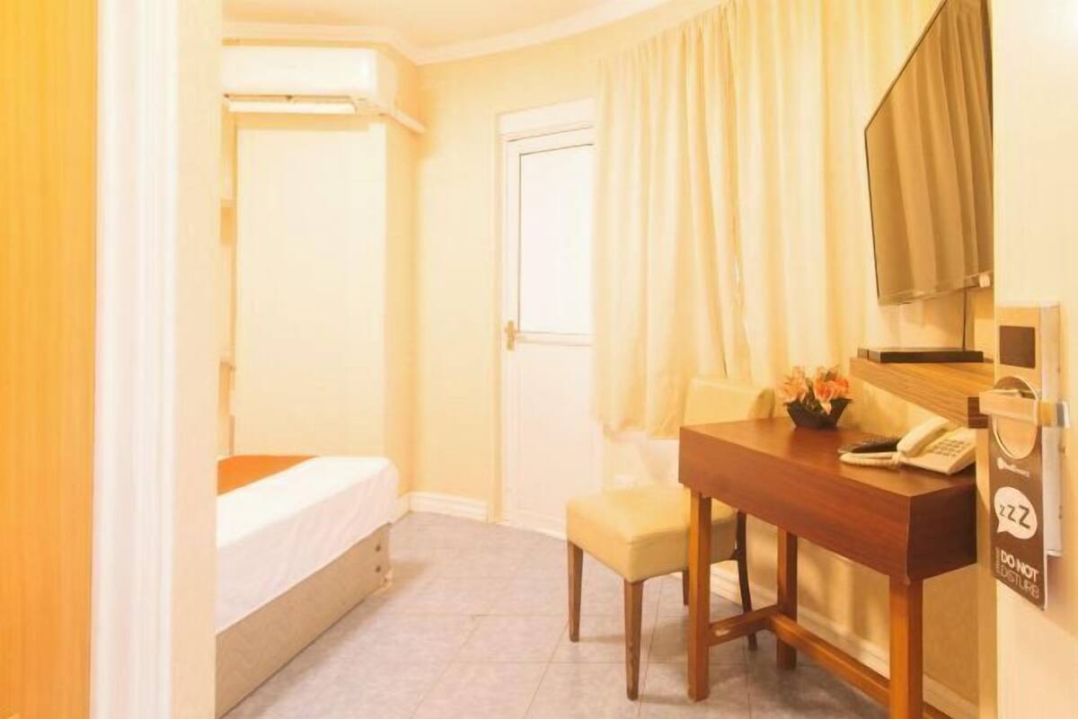 Una habitación de hotel con cama, escritorio, teléfono, silla y ventana con cortinas.