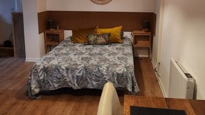 A bedroom with a bed, a wooden headboard, a bedside table, a lamp, a wall decoration, and a radiator. - Coquette and independent room, 2 steps from Chambord, the castles and Beauval (Tour-en-Sologne)