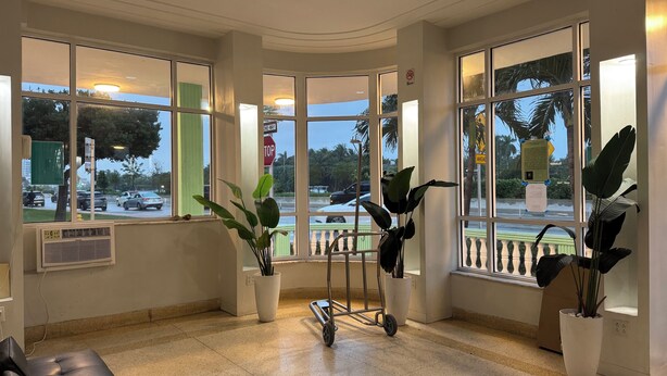 A waiting area with large windows, a black leather bench, and potted plants. - Lovely studio 3 Minute Walk to Miami Beach (Miami Beach)